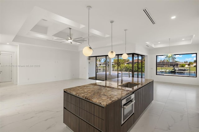 kitchen featuring ceiling fan, a large island, dark stone countertops, oven, and a tray ceiling