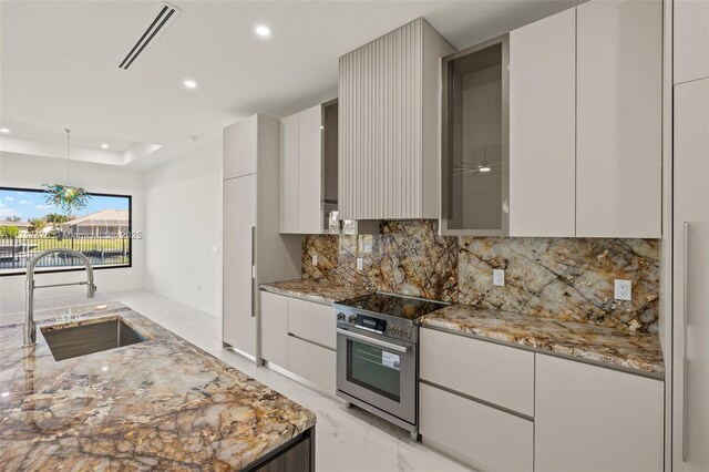 kitchen featuring sink, light stone counters, decorative light fixtures, a tray ceiling, and stainless steel stove