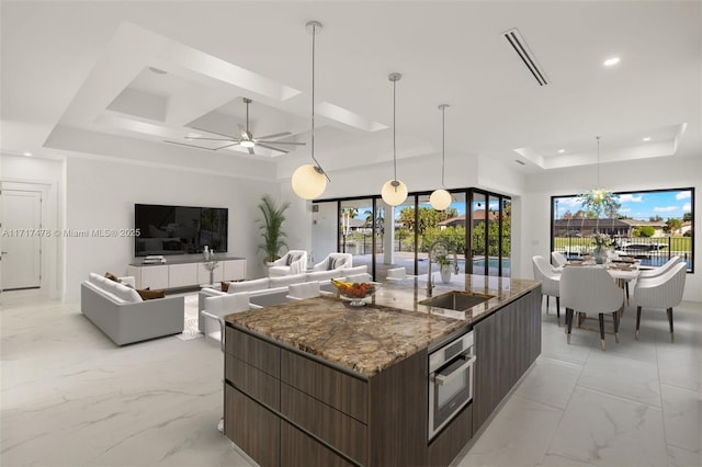 kitchen featuring dark brown cabinetry, oven, a raised ceiling, and a large island with sink