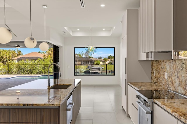 kitchen with stainless steel electric range oven, sink, light stone counters, a tray ceiling, and hanging light fixtures