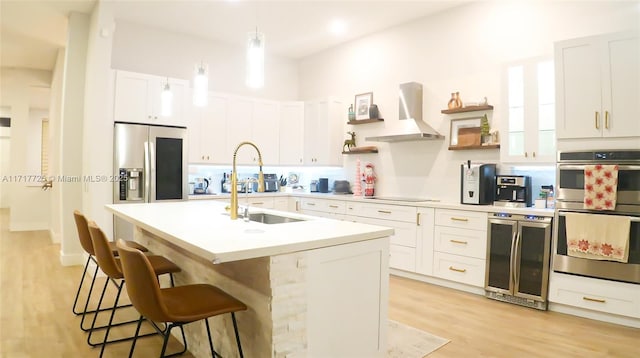 kitchen with appliances with stainless steel finishes, ventilation hood, a kitchen island with sink, pendant lighting, and white cabinets