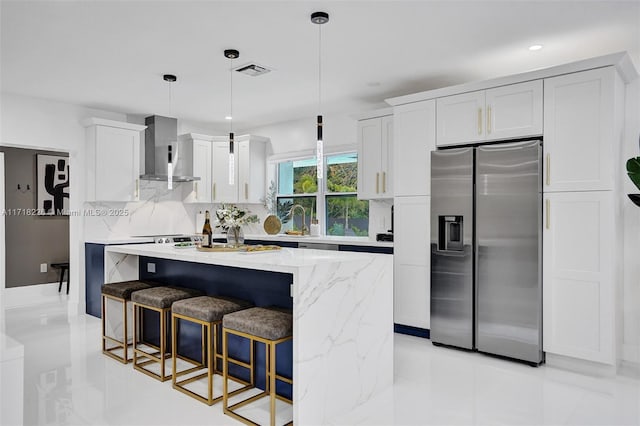 kitchen featuring white cabinetry, wall chimney range hood, stainless steel fridge with ice dispenser, pendant lighting, and a kitchen island