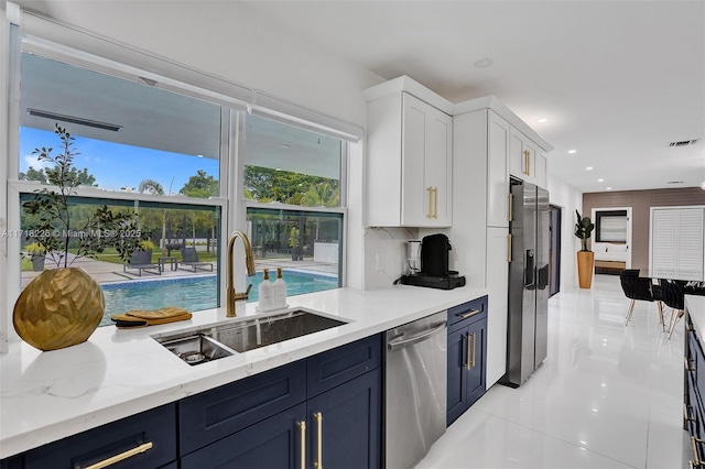 kitchen with light stone countertops, sink, blue cabinets, white cabinets, and appliances with stainless steel finishes