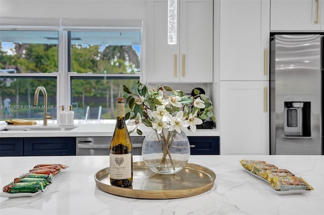 details featuring white cabinetry, stainless steel fridge with ice dispenser, sink, and light stone countertops