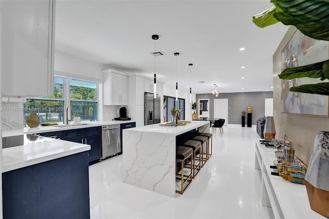 kitchen with pendant lighting, sink, appliances with stainless steel finishes, a kitchen island, and white cabinetry