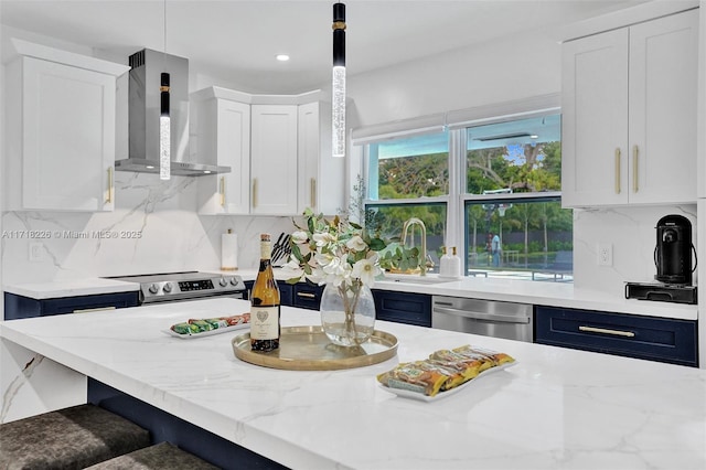 kitchen with white cabinets, wall chimney range hood, sink, hanging light fixtures, and appliances with stainless steel finishes