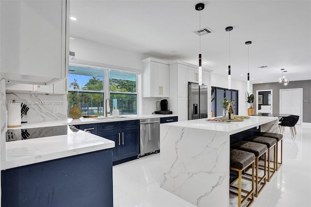 kitchen with appliances with stainless steel finishes, blue cabinetry, decorative light fixtures, white cabinetry, and a kitchen island