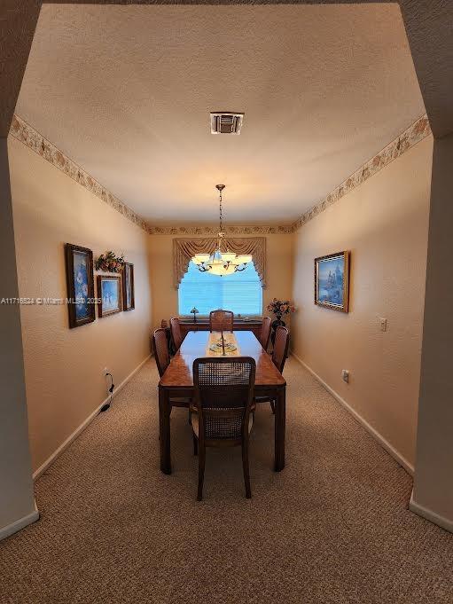 dining space featuring a textured ceiling, carpet floors, and a notable chandelier