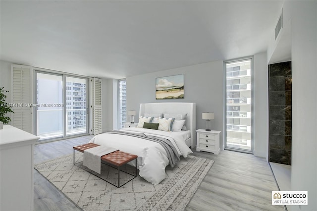 bedroom with access to exterior, light wood-type flooring, and expansive windows