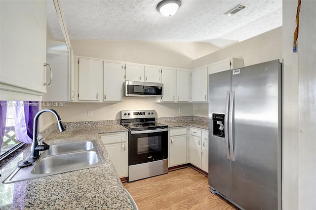 kitchen featuring white cabinets, appliances with stainless steel finishes, vaulted ceiling, and sink