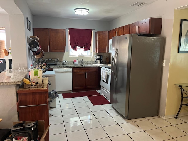 kitchen with light stone countertops, light tile patterned floors, white appliances, and sink