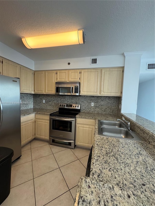 kitchen featuring light tile patterned floors, appliances with stainless steel finishes, light brown cabinets, tasteful backsplash, and sink