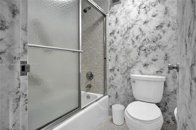 bathroom featuring tile patterned flooring, bath / shower combo with glass door, and toilet