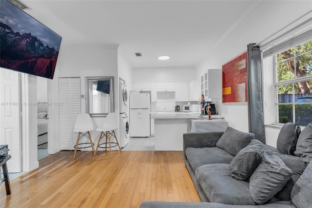 living room featuring ornamental molding, light hardwood / wood-style floors, and stacked washer and clothes dryer