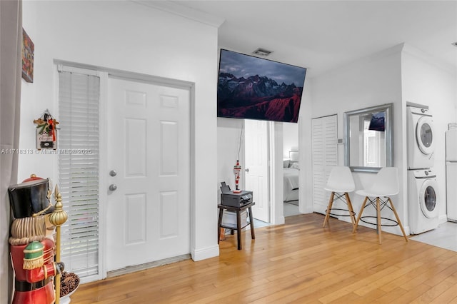 entrance foyer featuring wood-type flooring, ornamental molding, and stacked washer / drying machine