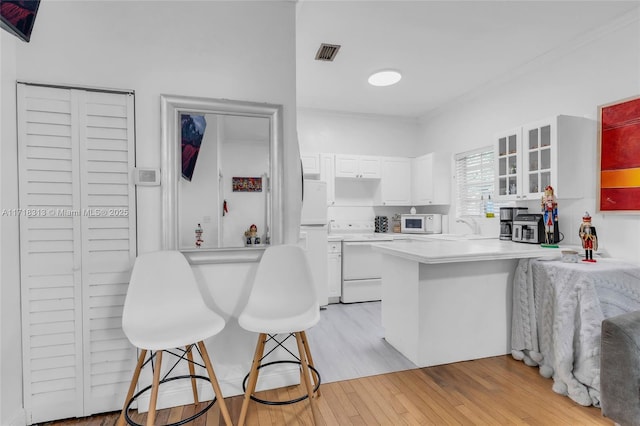 kitchen featuring kitchen peninsula, white appliances, light hardwood / wood-style flooring, white cabinetry, and a breakfast bar area