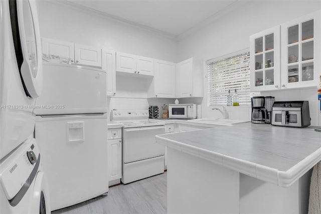 kitchen featuring kitchen peninsula, white appliances, sink, stacked washer and dryer, and white cabinetry