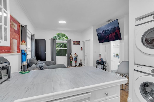 washroom with light hardwood / wood-style floors, crown molding, and stacked washer / dryer