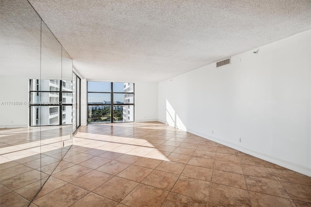 spare room featuring tile patterned flooring, expansive windows, visible vents, and a textured ceiling