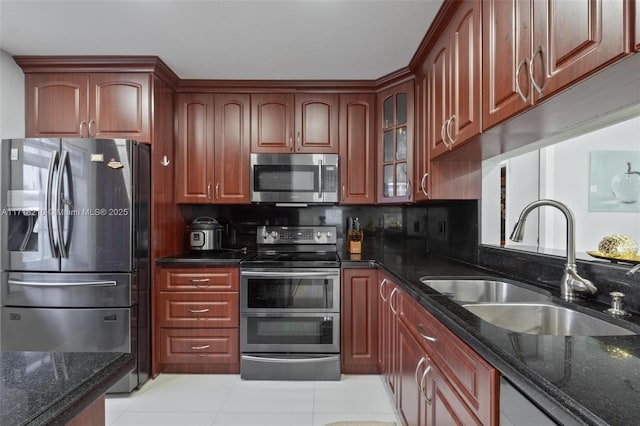 kitchen featuring appliances with stainless steel finishes, light tile patterned floors, dark stone counters, and sink