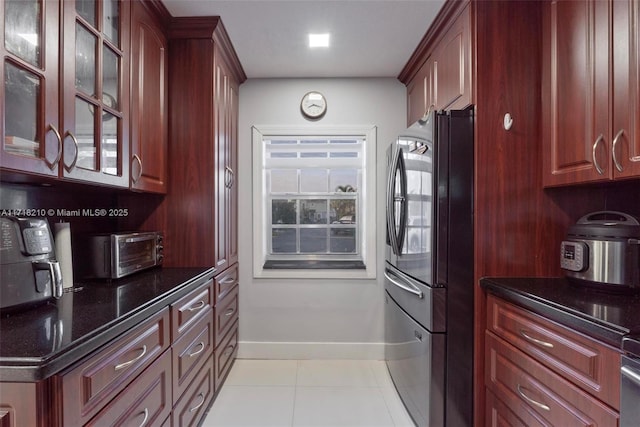 kitchen featuring stainless steel fridge, dark stone counters, and light tile patterned flooring