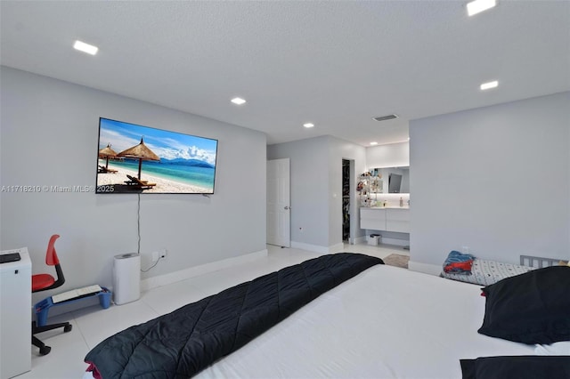 bedroom with ensuite bathroom, light tile patterned floors, and a textured ceiling