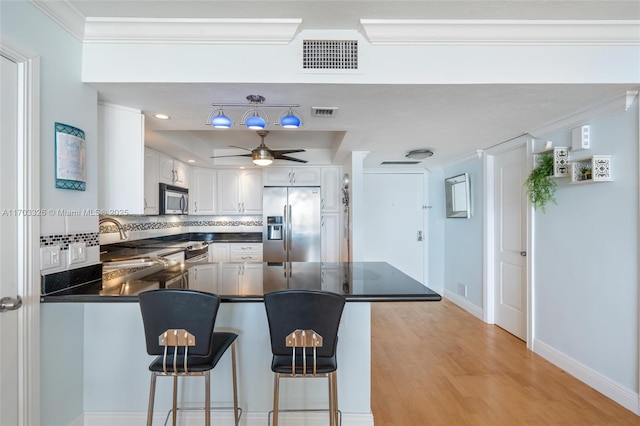 kitchen with white cabinets, a kitchen breakfast bar, decorative backsplash, appliances with stainless steel finishes, and kitchen peninsula