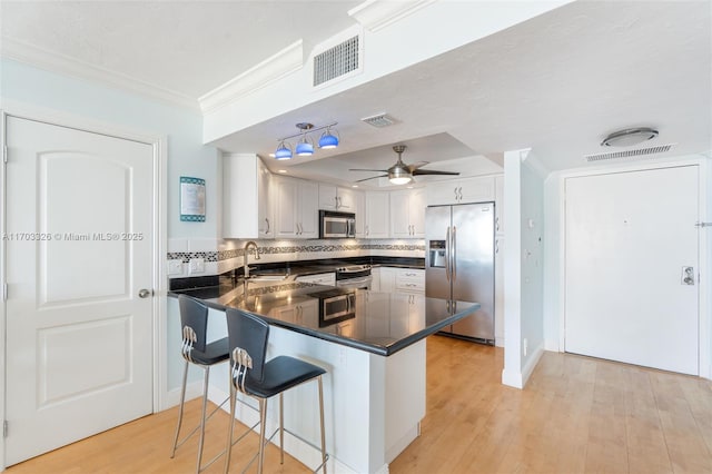 kitchen featuring tasteful backsplash, kitchen peninsula, a kitchen bar, white cabinets, and appliances with stainless steel finishes