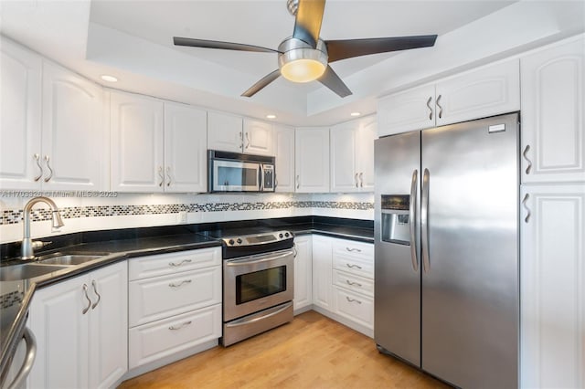 kitchen with stainless steel appliances, white cabinetry, a tray ceiling, and sink