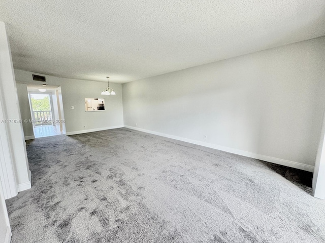 carpeted spare room with a notable chandelier and a textured ceiling