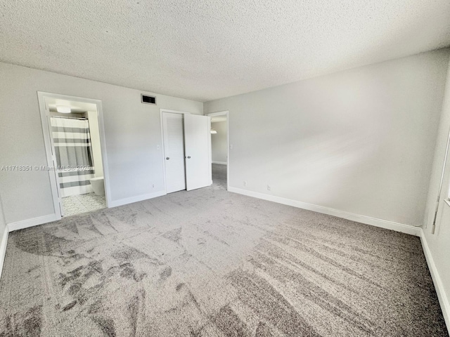 unfurnished bedroom featuring carpet flooring, a closet, a textured ceiling, and ensuite bath