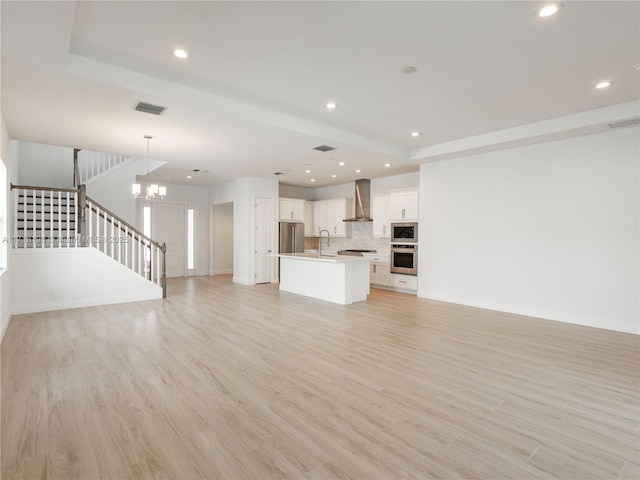 unfurnished living room featuring sink, an inviting chandelier, and light hardwood / wood-style flooring