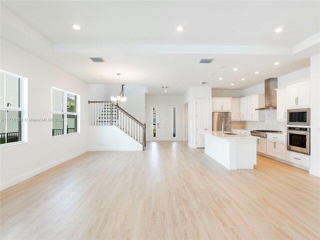 kitchen featuring a kitchen island with sink, white cabinets, wall chimney range hood, light hardwood / wood-style floors, and stainless steel appliances