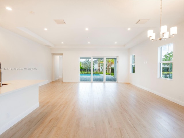 unfurnished room featuring a tray ceiling, light hardwood / wood-style floors, and a notable chandelier