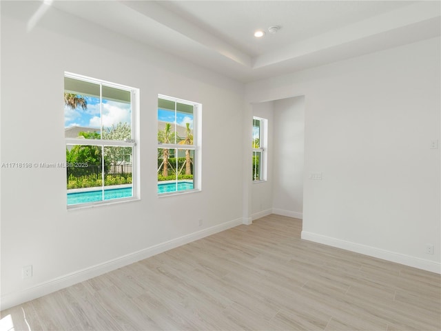 spare room with a tray ceiling and light hardwood / wood-style floors