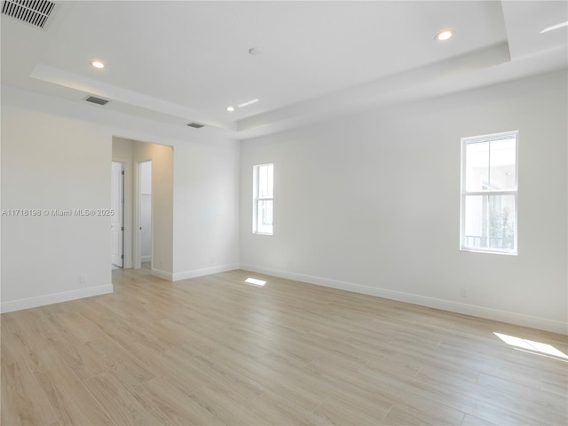 spare room featuring a tray ceiling and light wood-type flooring