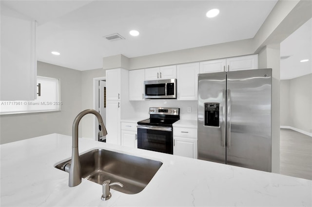 kitchen with white cabinets, appliances with stainless steel finishes, sink, and light stone counters