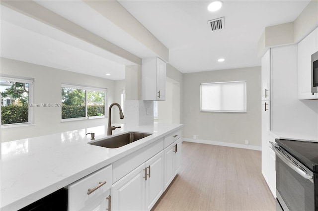 kitchen featuring white cabinetry, stainless steel electric range, light stone countertops, light hardwood / wood-style flooring, and sink