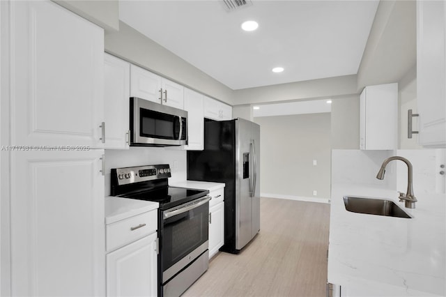 kitchen with appliances with stainless steel finishes, light hardwood / wood-style flooring, white cabinetry, and sink