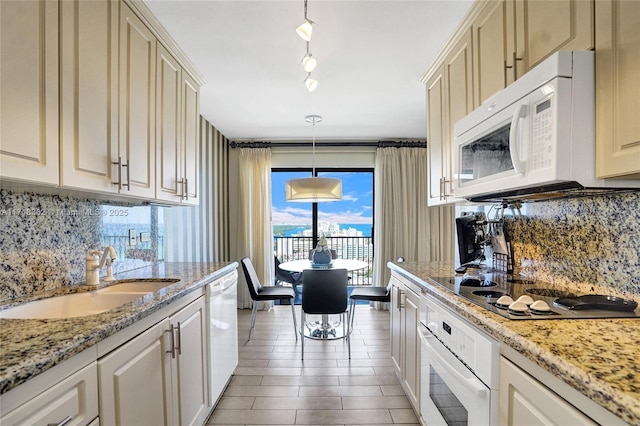 kitchen with track lighting, light stone counters, white appliances, sink, and pendant lighting