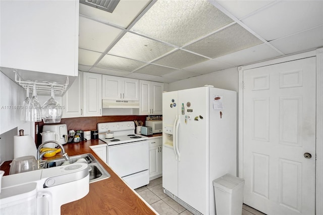 kitchen featuring a paneled ceiling, white appliances, sink, light tile patterned floors, and white cabinetry