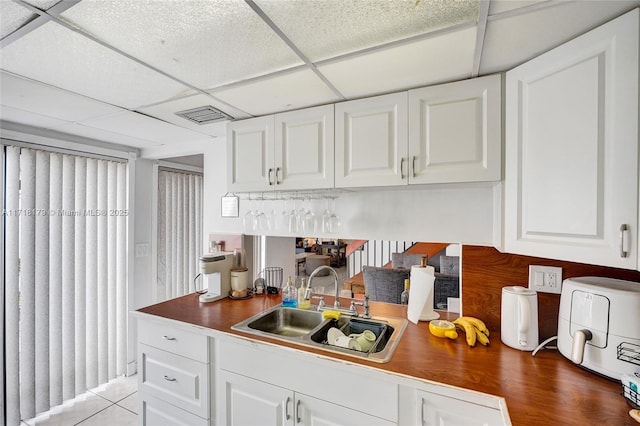 kitchen featuring a paneled ceiling, sink, and white cabinets