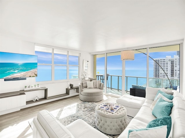 living room featuring floor to ceiling windows, a water view, a healthy amount of sunlight, and light hardwood / wood-style flooring