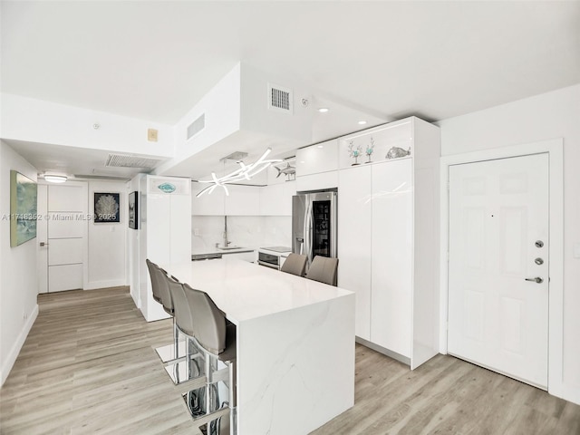 kitchen with stainless steel fridge, white cabinets, a kitchen breakfast bar, and light hardwood / wood-style floors