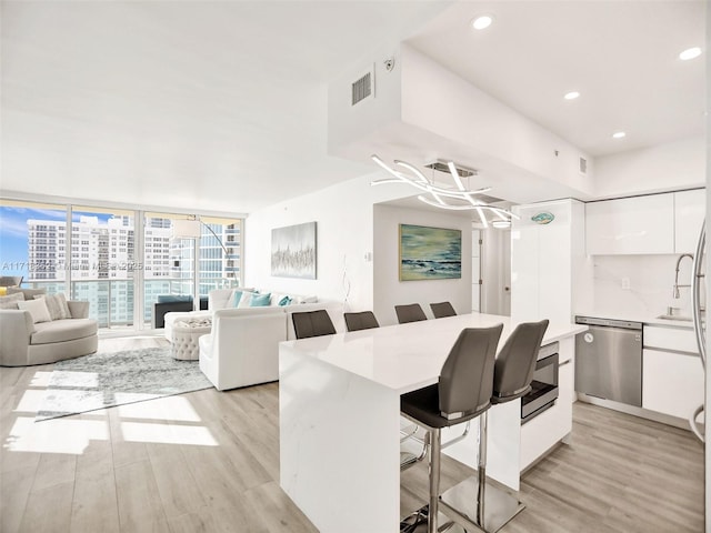 kitchen featuring a breakfast bar area, light hardwood / wood-style floors, expansive windows, white cabinets, and stainless steel dishwasher