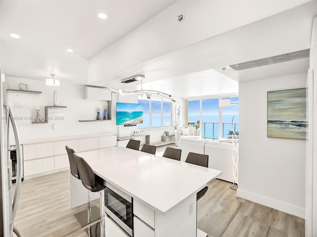 kitchen with built in microwave, a center island, white cabinets, and light hardwood / wood-style floors