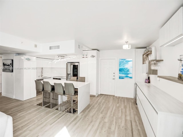 kitchen with a kitchen island, white cabinetry, a kitchen breakfast bar, light hardwood / wood-style floors, and stainless steel fridge with ice dispenser