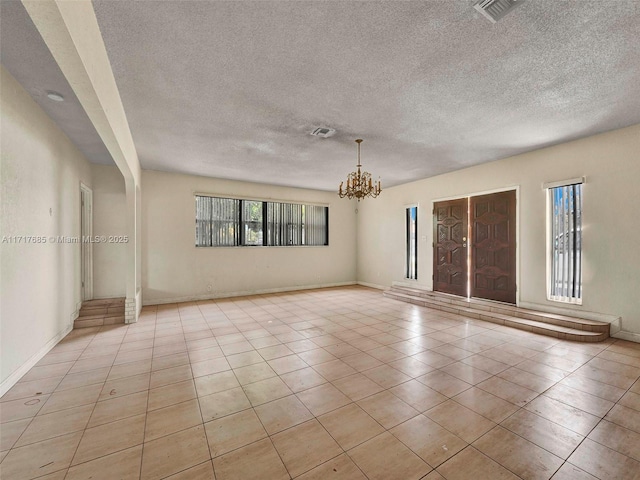 tiled empty room with a textured ceiling and a notable chandelier