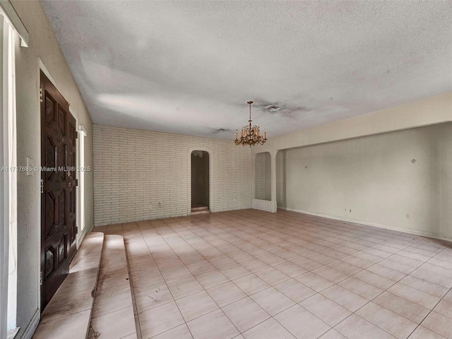 unfurnished room featuring a chandelier, light tile patterned flooring, brick wall, and a textured ceiling