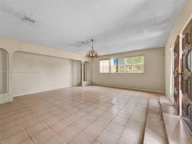 empty room featuring light tile patterned floors, a textured ceiling, and an inviting chandelier